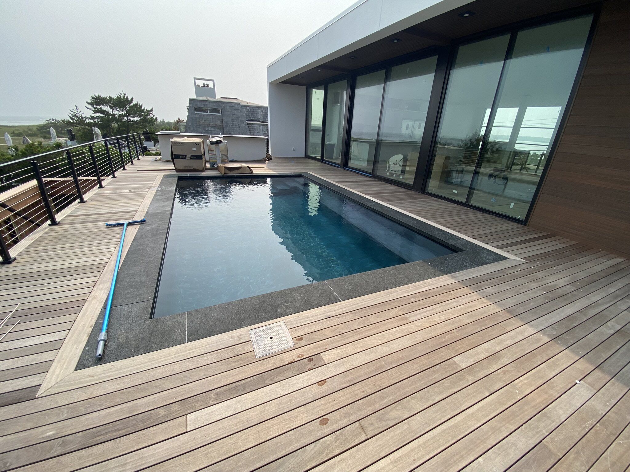 Modern gunite pool with wood decking beside a glass-walled home on Long Island