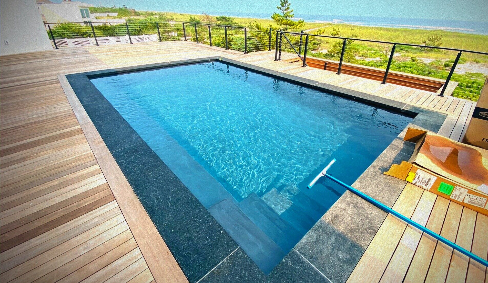 Gunite pool with dark tile and wood deck near the beach